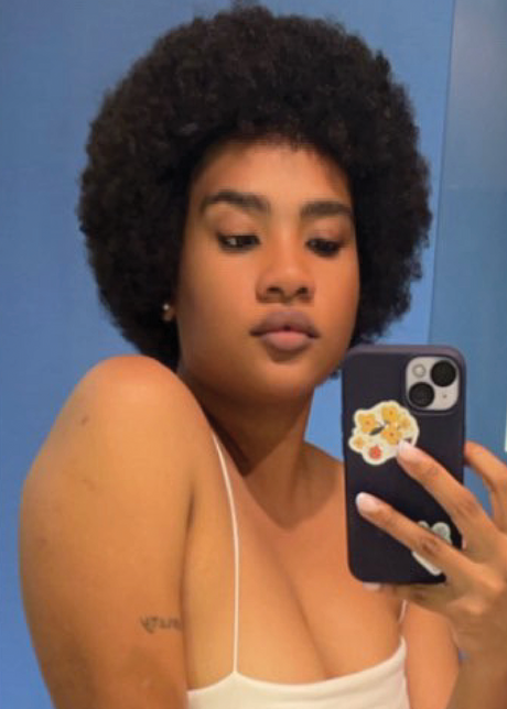 Person with an afro hairstyle taking a mirror selfie with a phone.