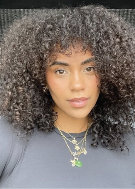 A person with curly hair wearing layered necklaces and a black top.