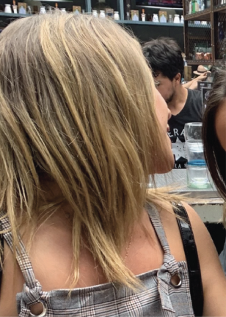 Woman with shoulder-length blond hair sitting in an outdoor café, background shows shelves with various items.
